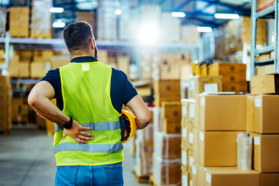 A warehouse worker having back pain and rubbing it